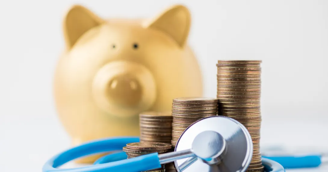 A piggy bank next to a pile of coins and a stethoscope A piggy bank next to a pile of coins and a stethoscope