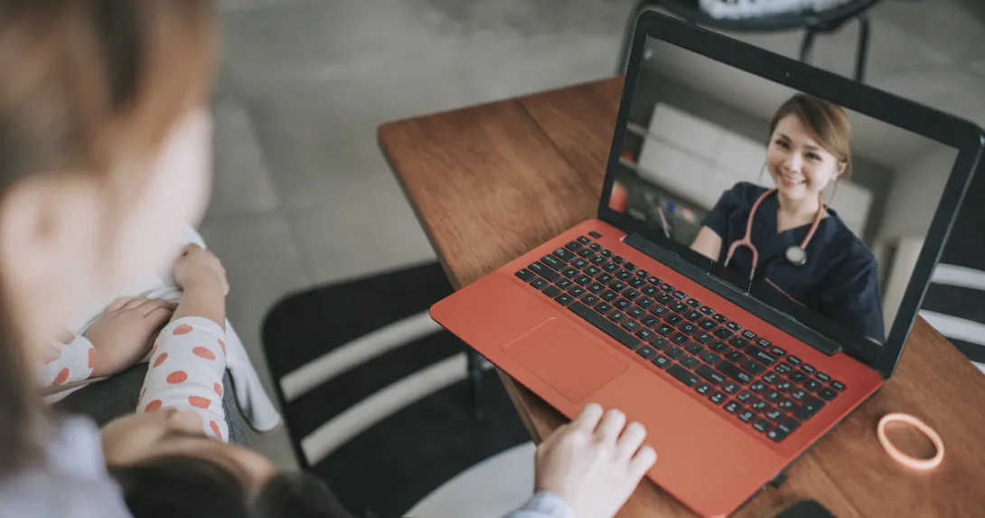 Two people sitting on a couch while looking at an orange and black computer and speaking with a virtual healthcare provider Two people sitting on a couch while looking at an orange and black computer and speaking with a virtual healthcare provider