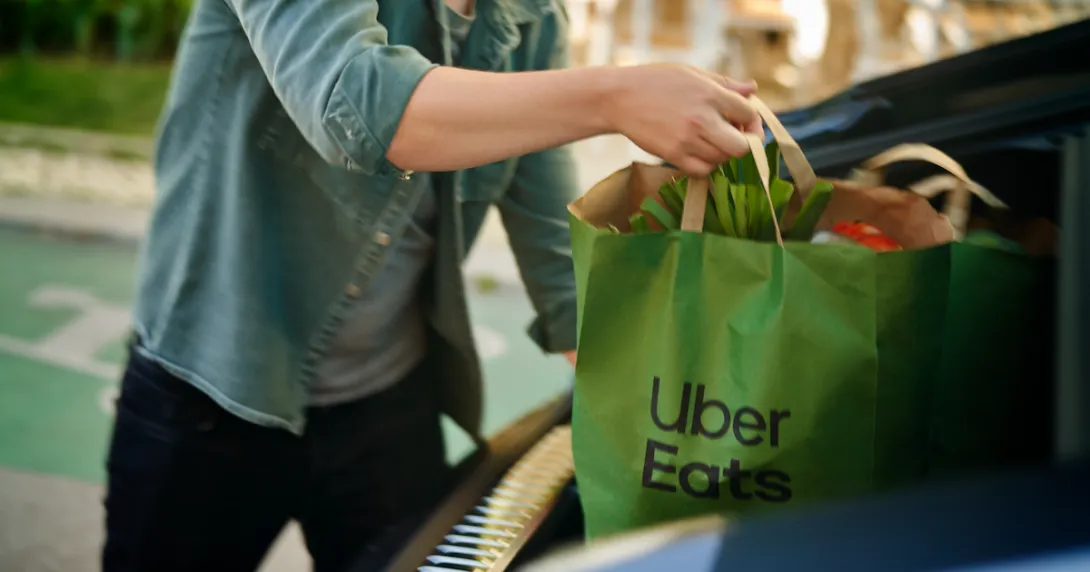 Person putting a bag of groceries from Uber Eats in a car's trunk Person putting a bag of groceries from Uber Eats in a car's trunk
