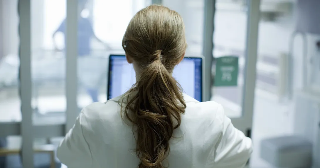 Woman doctor with long red hair using laptop in hospital, photographed from behind Woman doctor with long red hair using laptop in hospital, photographed from behind