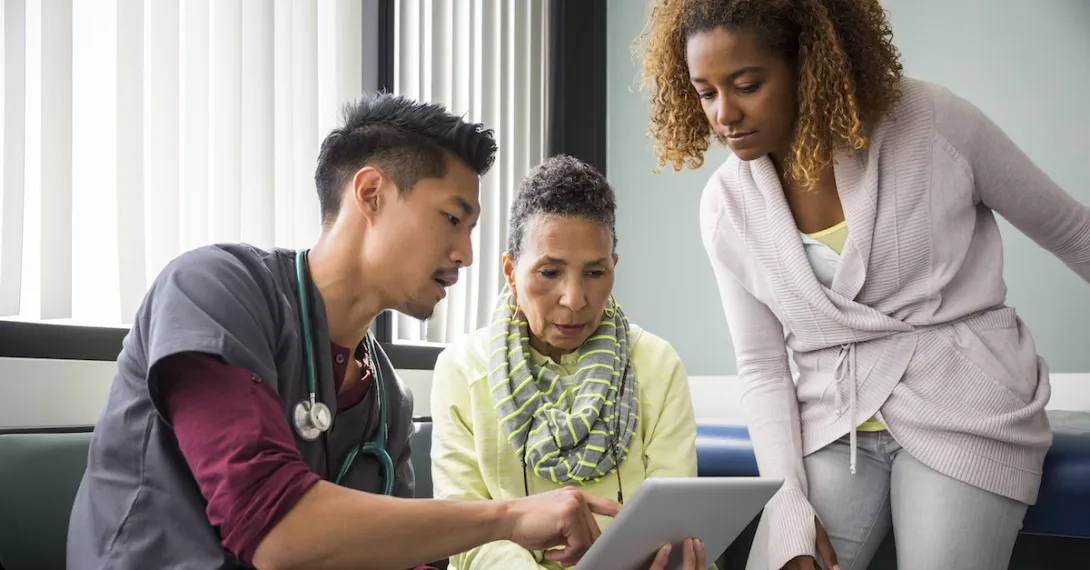 A doctor using a tablet while talking to a patient and her family member. A doctor using a tablet while talking to a patient and her family member.