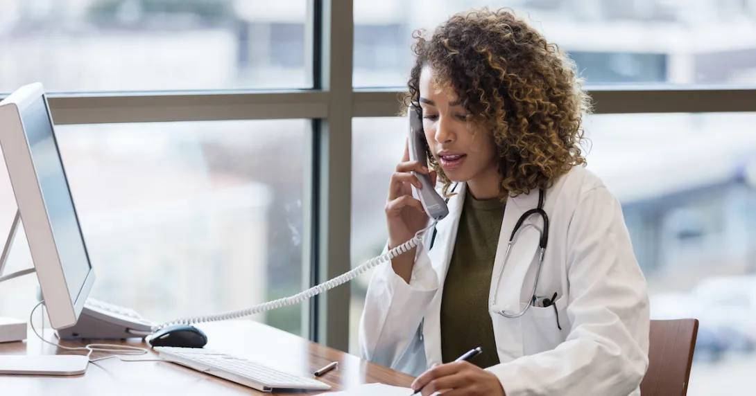 A doctor, sitting in her office, uses the landline to make phone calls regarding patient records. A doctor, sitting in her office, uses the landline to make phone calls regarding patient records.