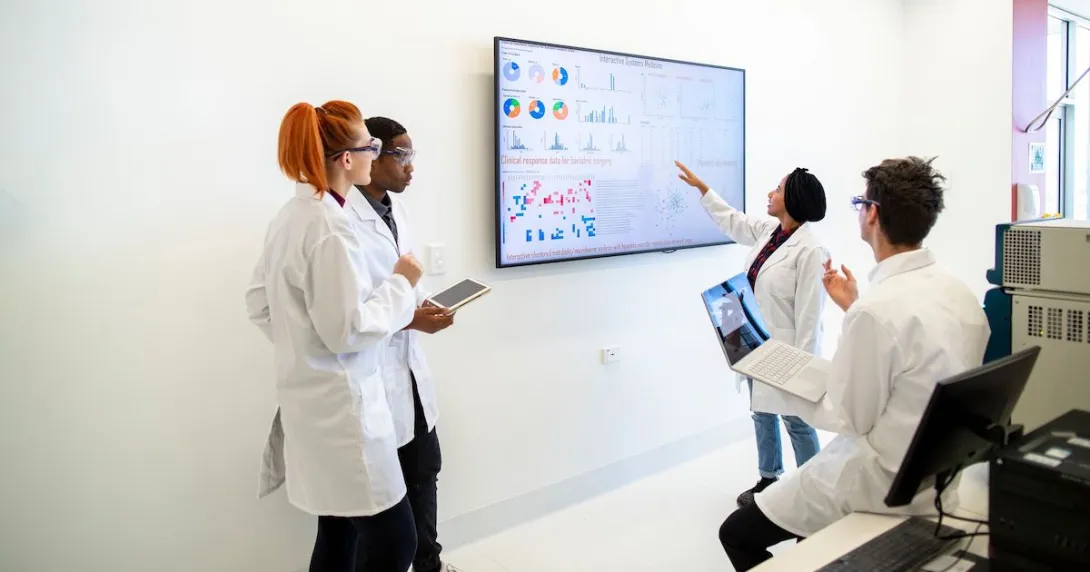 A group of providers or researchers looking at a data dashboard on a large TV on a wall A group of providers or researchers looking at a data dashboard on a large TV on a wall