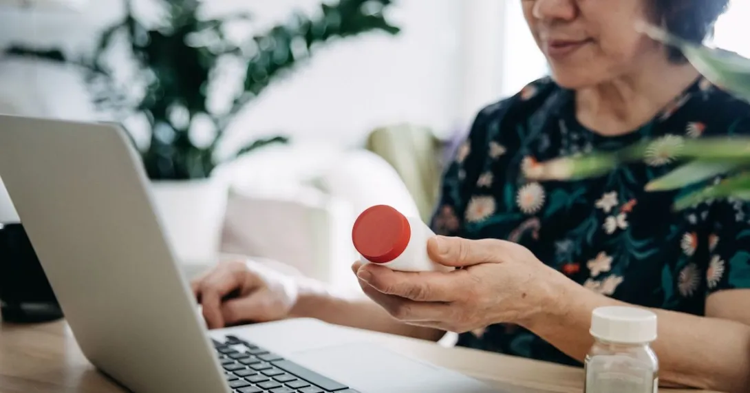 A close up of a woman holding a prescription bottle while using a laptop A close up of a woman holding a prescription bottle while using a laptop