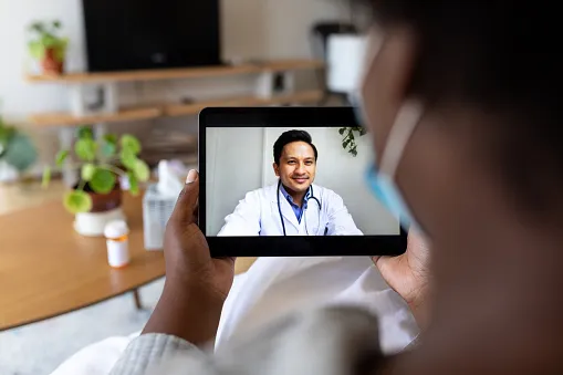 Person holding up a tablet with a telehealth provider on the screen Person holding up a tablet with a telehealth provider on the screen