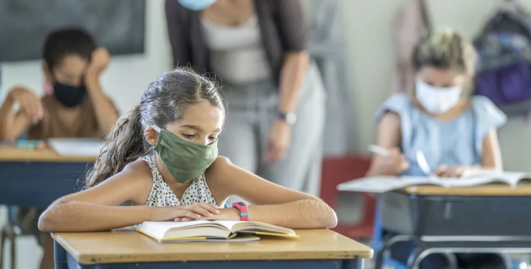 12 year old girl wearing a reusable, protective face mask in classroom while working on school work at her desk. 12 year old girl wearing a reusable, protective face mask in classroom while working on school work at her desk.