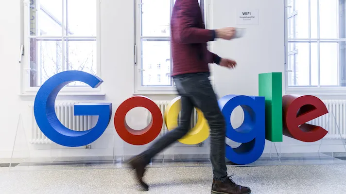 A person walking past a Google sign in an office A person walking past a Google sign in an office