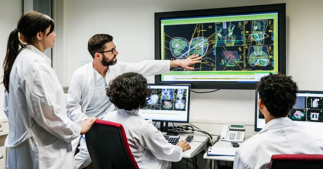A group of doctors discussing a patient's test results on a large monitor in an office. A group of doctors discussing a patient's test results on a large monitor in an office.