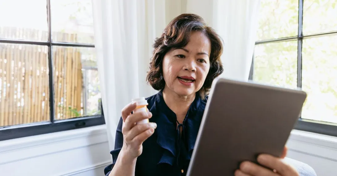 Person on a tablet holding a prescription bottle in their hand while sitting next to a window