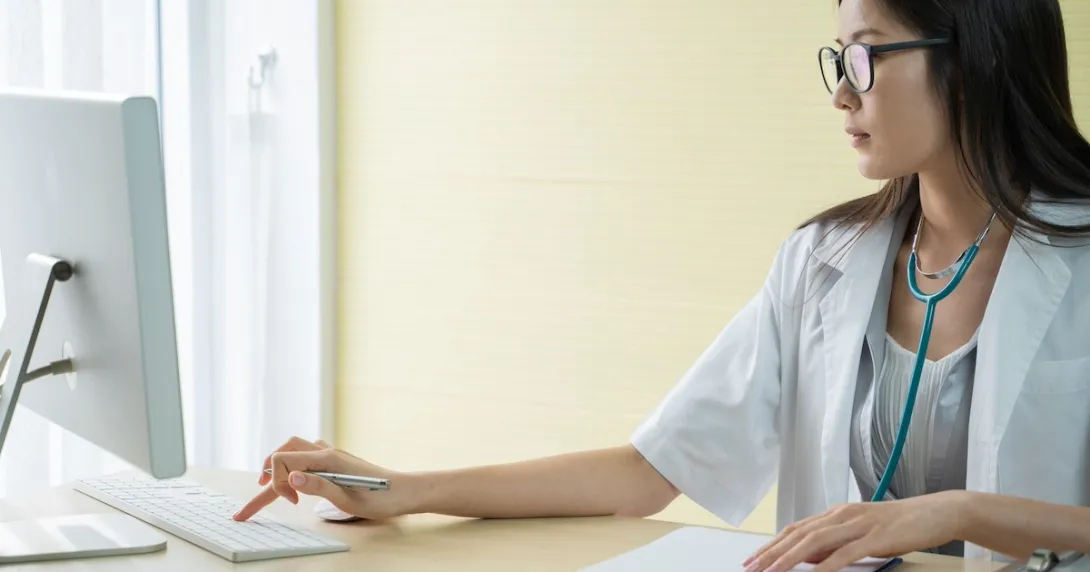 Healthcare provider sitting at a desk wearing a stethoscope around their neck and working on a computer Healthcare provider sitting at a desk wearing a stethoscope around their neck and working on a computer