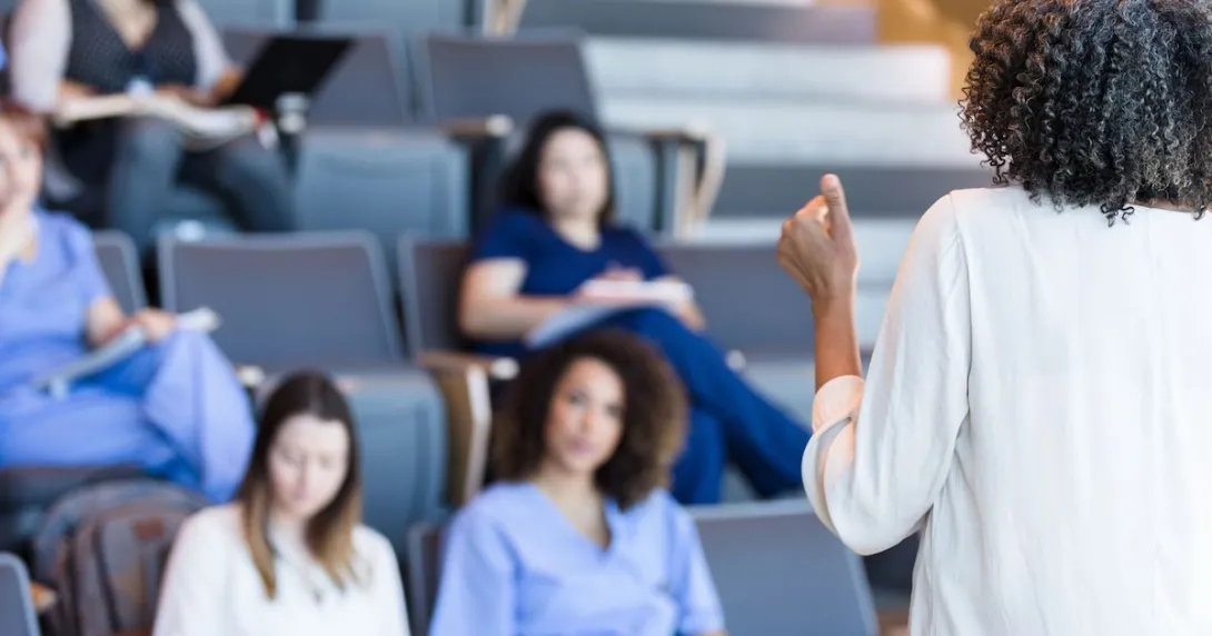 Students in scrubs sitting in a classroom looking at a teacher Students in scrubs sitting in a classroom looking at a teacher