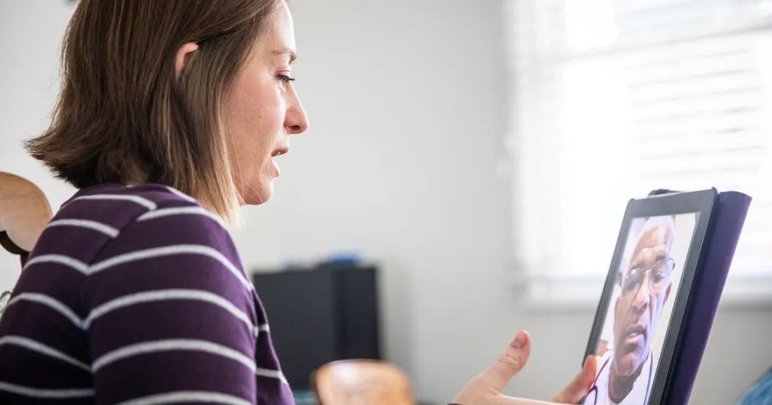 Person sitting at a computer speaking to a healthcare provider on the screen Person sitting at a computer speaking to a healthcare provider on the screen
