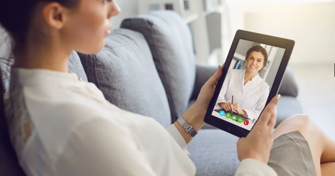 Person sitting on their couch speaking to a healthcare professional on a tablet Person sitting on their couch speaking to a healthcare professional on a tablet