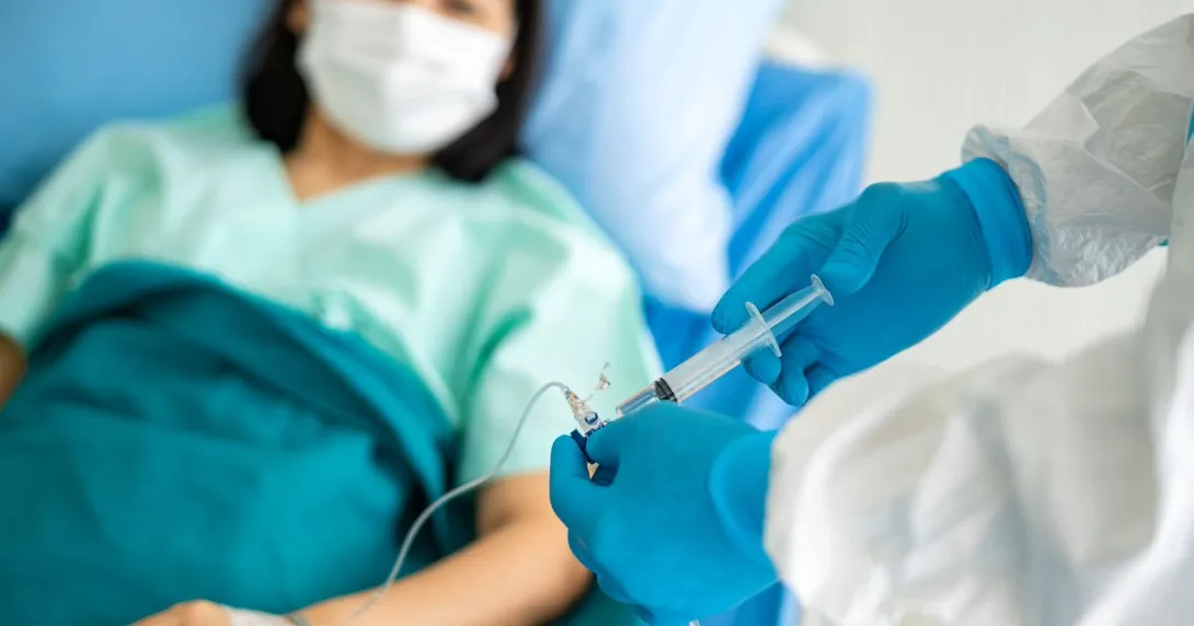Healthcare provider putting medication into an infusion line with a patient lying in a bed Healthcare provider putting medication into an infusion line with a patient lying in a bed