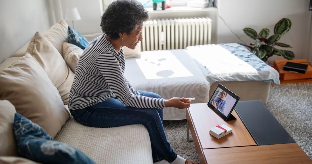Person sitting on their couch speaking to a healthcare provider on a tablet Person sitting on their couch speaking to a healthcare provider on a tablet