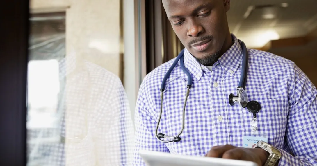 Healthcare provider standing next to a window while looking at a tablet Healthcare provider standing next to a window while looking at a tablet
