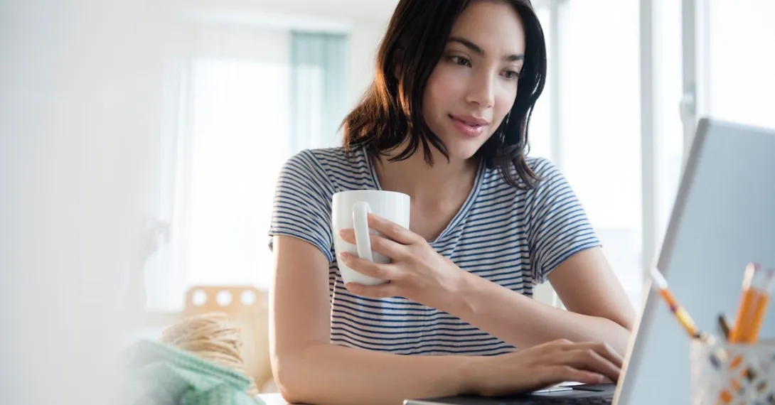 Person sitting at their computer while holding a cup of coffee Person sitting at their computer while holding a cup of coffee