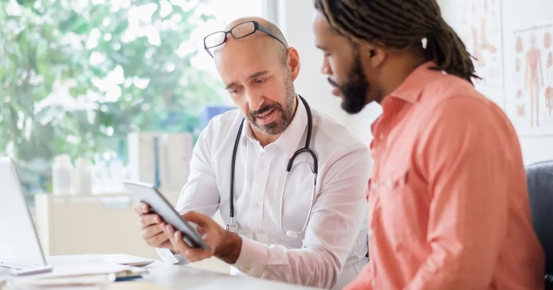 Healthcare provider and patient with an orange shirt sitting at a desk and looking at a tablet Healthcare provider and patient with an orange shirt sitting at a desk and looking at a tablet