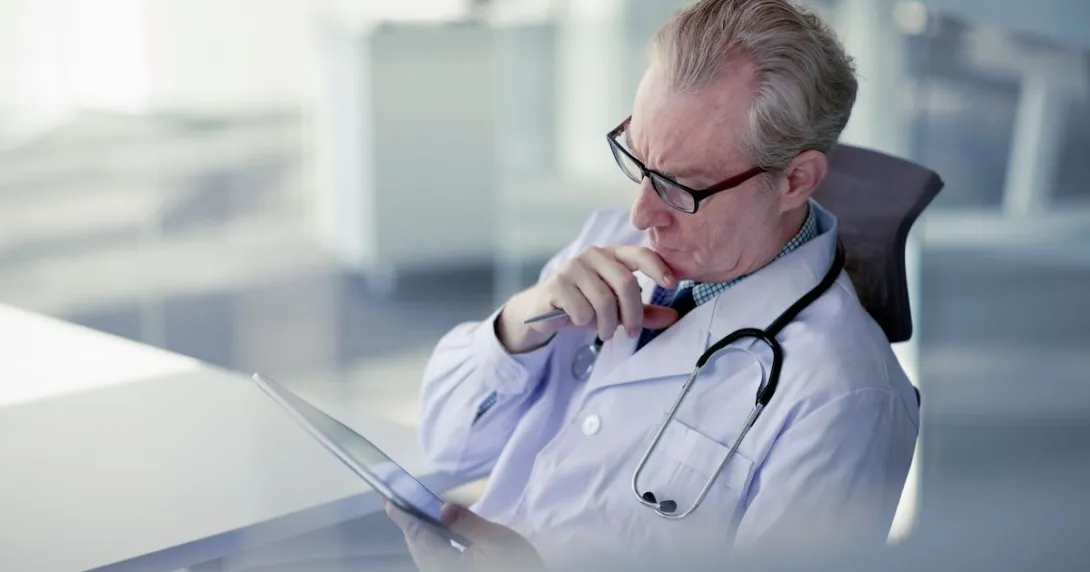 Healthcare provider looking at a tablet while holding their chin as though deep in thought Healthcare provider looking at a tablet while holding their chin as though deep in thought