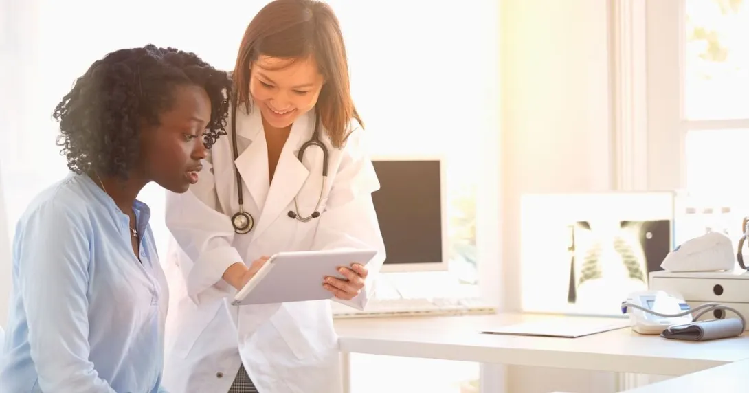 Healthcare provider standing over a patient sitting down while showing them a tablet