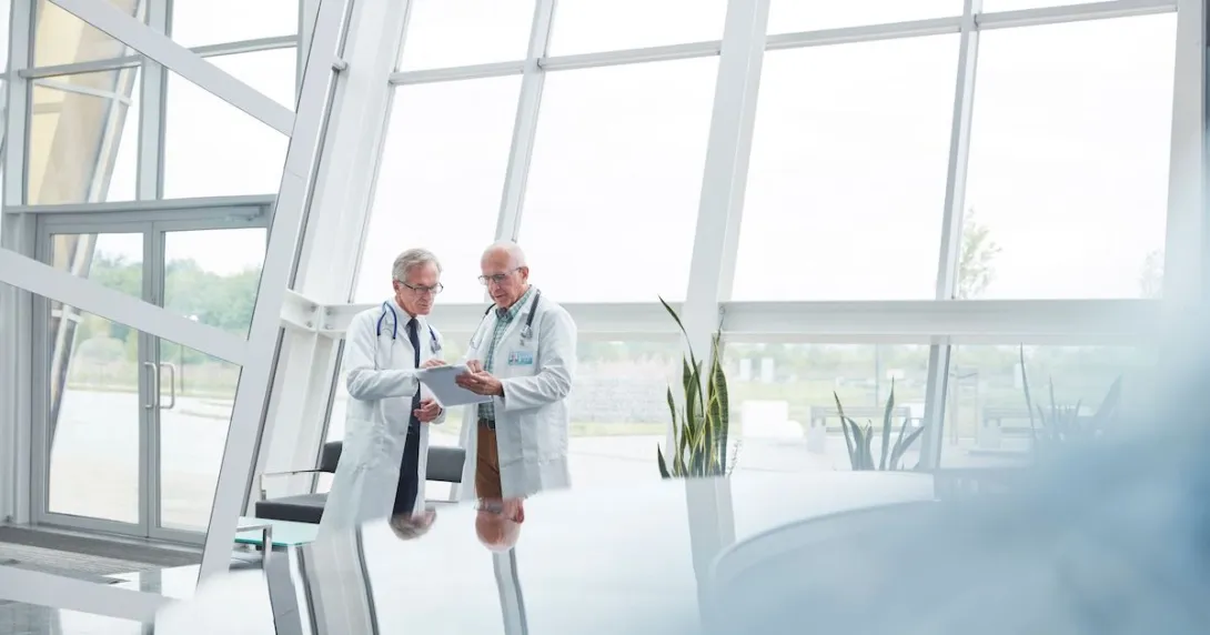 Two healthcare providers in a room with big windows Two healthcare providers in a room with big windows