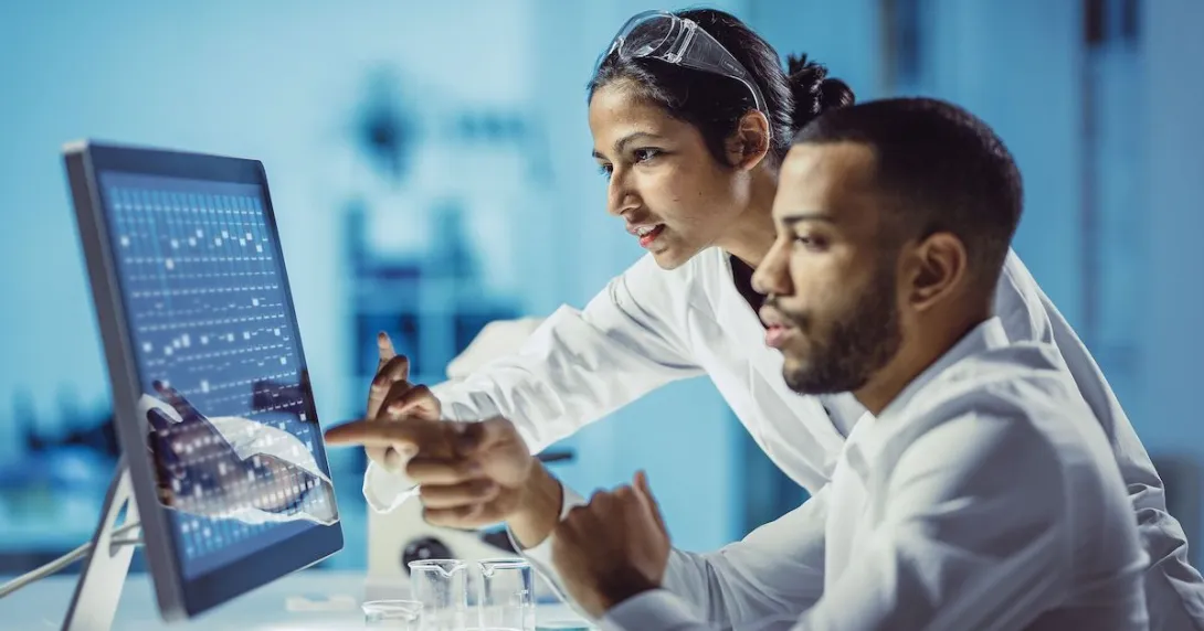 Two healthcare providers sitting in front of a computer touching the screen Two healthcare providers sitting in front of a computer touching the screen
