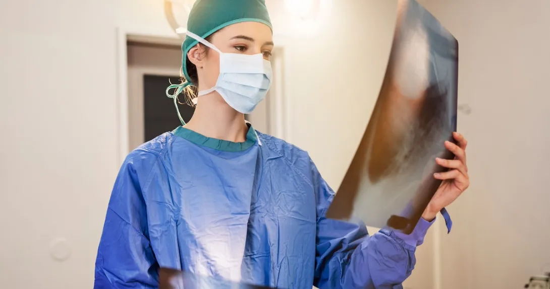 Healthcare provider in scrubs wearing a mask and looking at a large diagnostic image Healthcare provider in scrubs wearing a mask and looking at a large diagnostic image