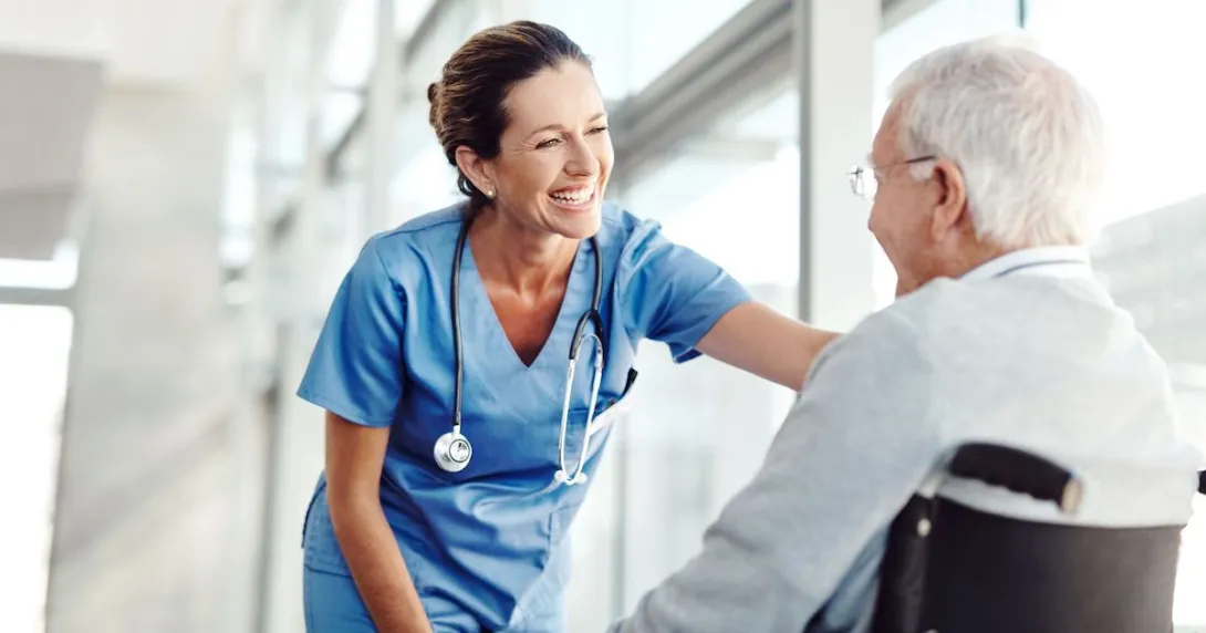 Person sitting in a wheelchair with a healthcare provider in scrubs standing over them Person sitting in a wheelchair with a healthcare provider in scrubs standing over them
