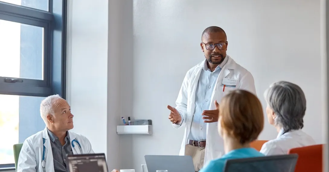 Healthcare provider standing in front of three other people in a meeting room Healthcare provider standing in front of three other people in a meeting room