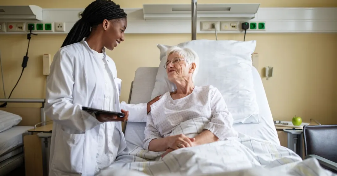 Healthcare provider standing next to a patient lying in a bed in a hospital room Healthcare provider standing next to a patient lying in a bed in a hospital room