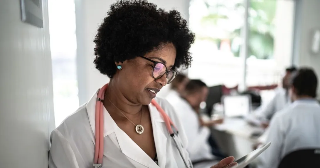 Healthcare provider standing in a hallway looking at a tablet Healthcare provider standing in a hallway looking at a tablet