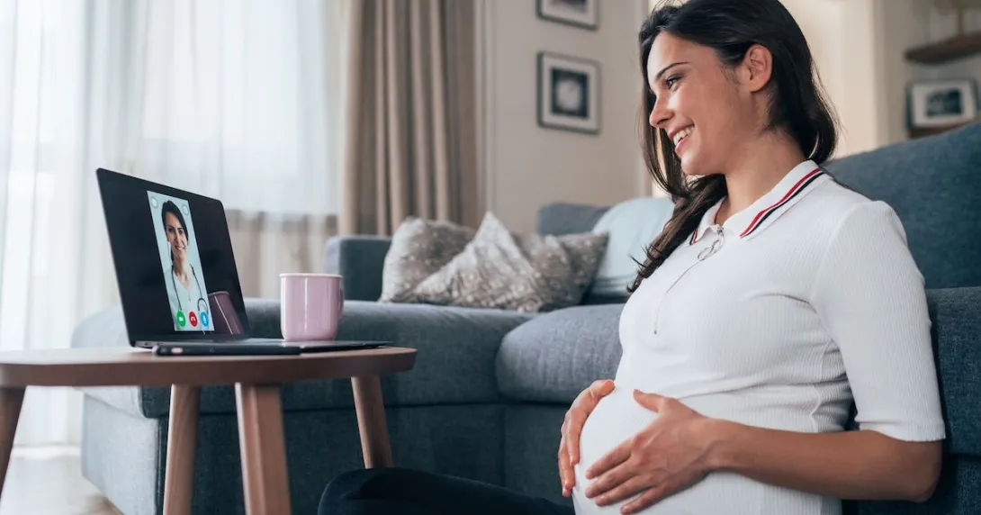 Person sitting on the floor while rubbing their pregnant belly and talking to a healthcare provider on a computer Person sitting on the floor while rubbing their pregnant belly and talking to a healthcare provider on a computer