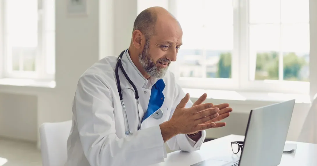Healthcare provider sitting at a desk and talking to someone on a computer Healthcare provider sitting at a desk and talking to someone on a computer