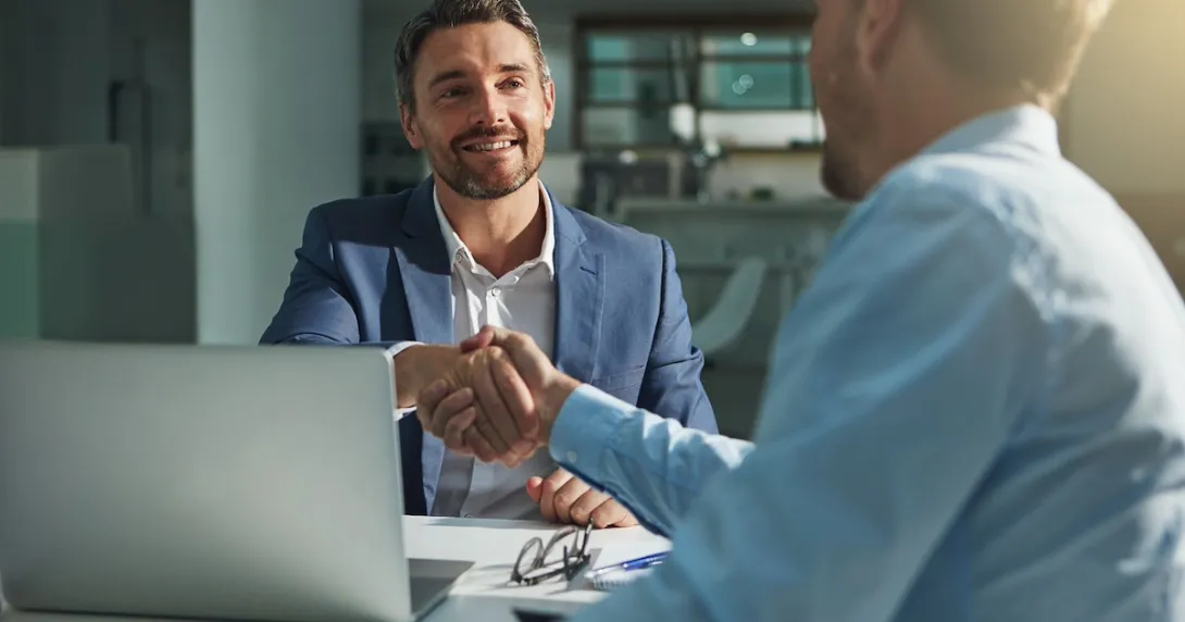 Two people sitting on opposite sides of a desk while shaking hands