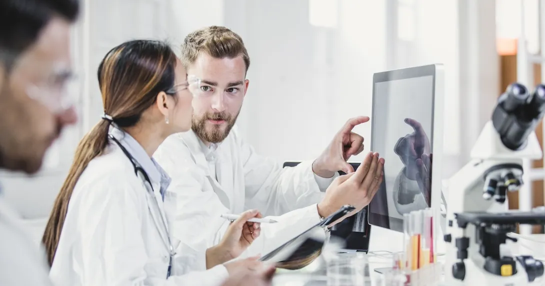 Three healthcare providers standing around a computer looking at the screen Three healthcare providers standing around a computer looking at the screen