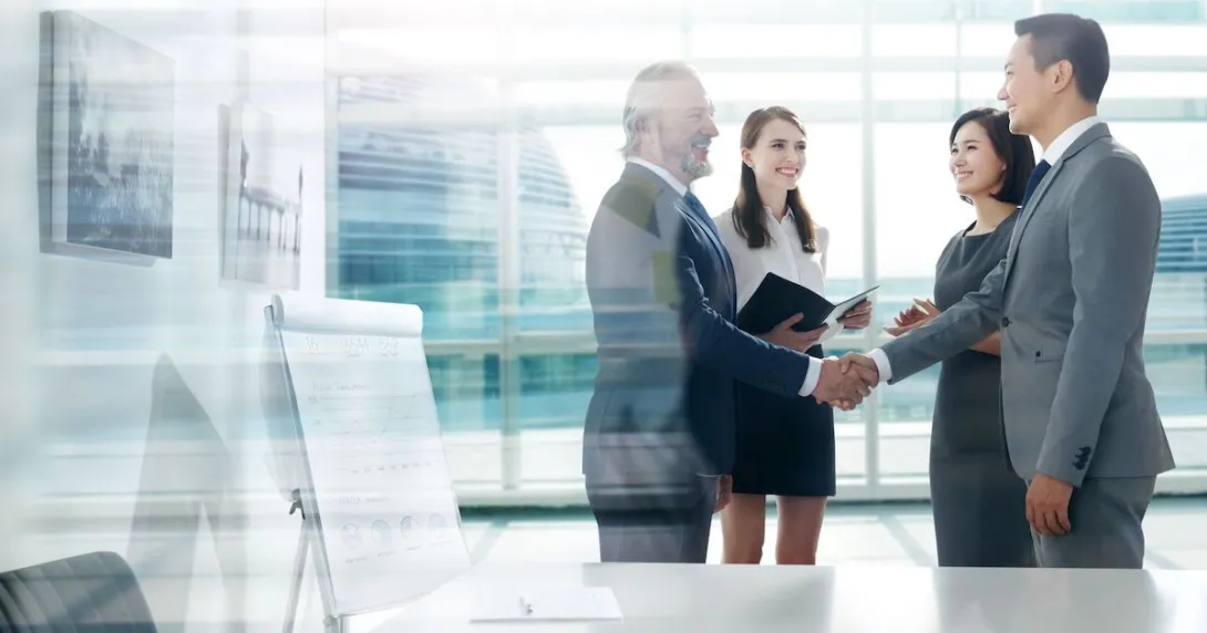 Four people standing in a room next to a large glass window with two of them shaking hands and the other two watching Four people standing in a room next to a large glass window with two of them shaking hands and the other two watching