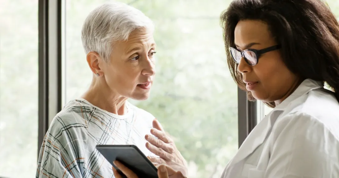 Healthcare provider standing next to a patient while looking at a tablet Healthcare provider standing next to a patient while looking at a tablet