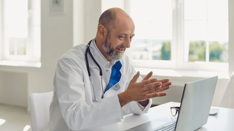 Healthcare provider sitting at a desk while looking at a laptop Healthcare provider sitting at a desk while looking at a laptop