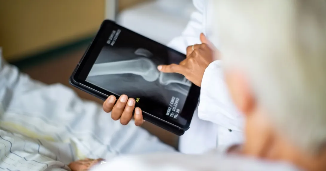 A doctor holding a digital tablet showing a patient their bone X-ray A doctor holding a digital tablet showing a patient their bone X-ray