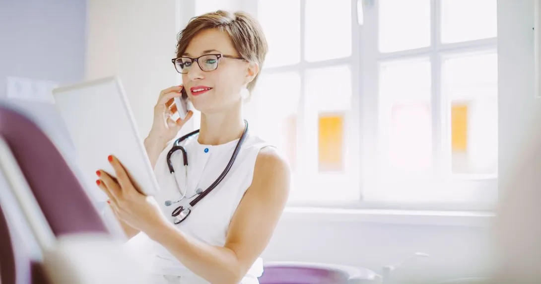 A doctor calling a fellow from their mobile phone while reviewing a patient's file on a digital tablet A doctor calling a fellow from their mobile phone while reviewing a patient's file on a digital tablet
