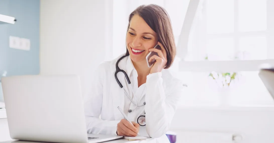 A doctor on the phone with a patient while checking their medical record on a laptop computer A doctor on the phone with a patient while checking their medical record on a laptop computer