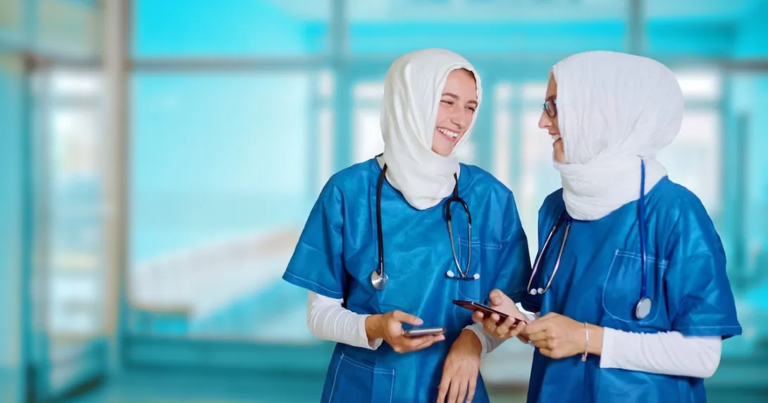 Nurses wearing hijabs conversing while holding their smartphones Nurses wearing hijabs conversing while holding their smartphones