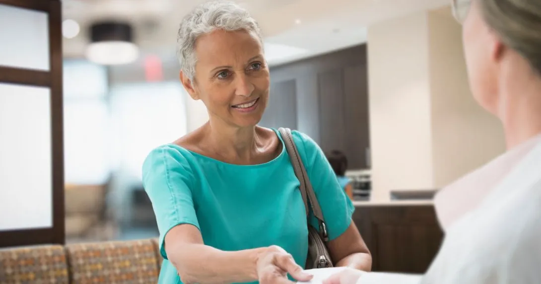 A person handing an insurance card to a front desk worker at a medical office A person handing an insurance card to a front desk worker at a medical office