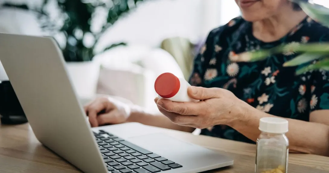 A close up of a person holding a pill bottle while using a laptop A close up of a person holding a pill bottle while using a laptop
