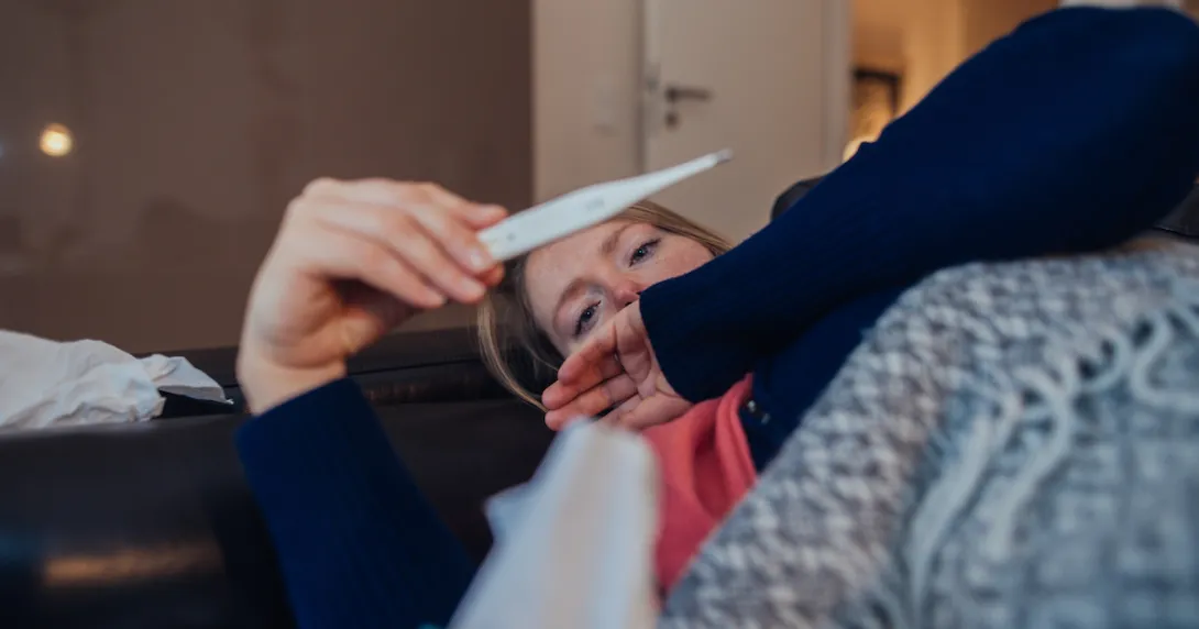 A sick woman looking at a thermometer A sick woman looking at a thermometer