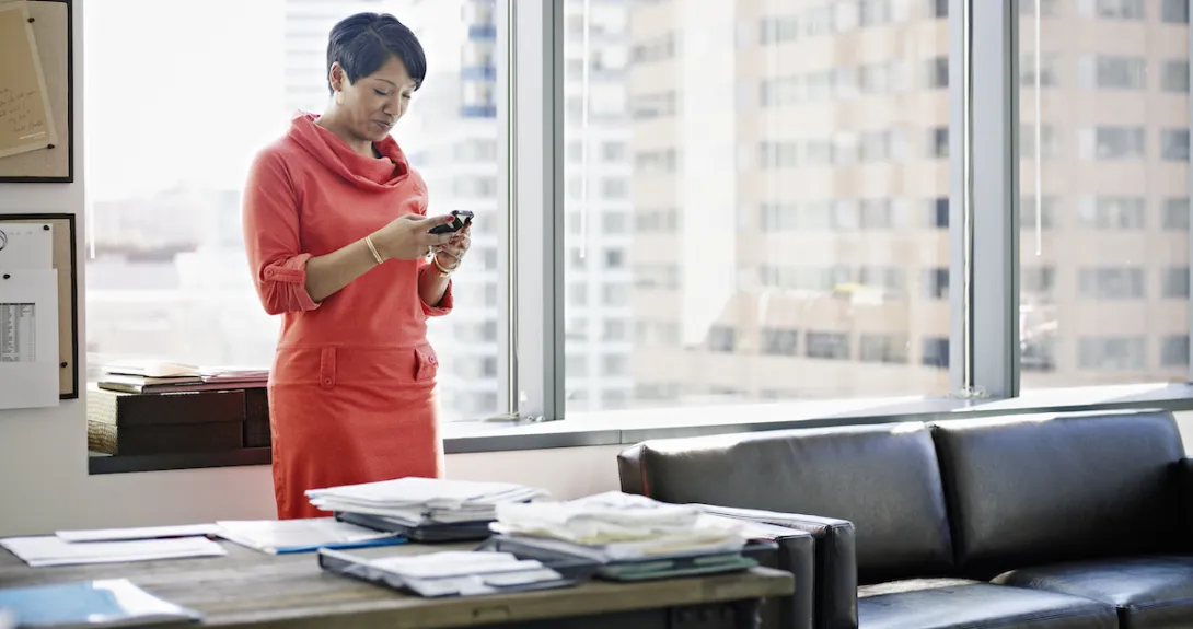 A person using a smartphone at her desk. A person using a smartphone at her desk.